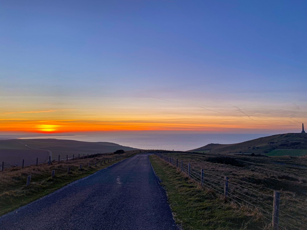 the sun is setting over a rural road