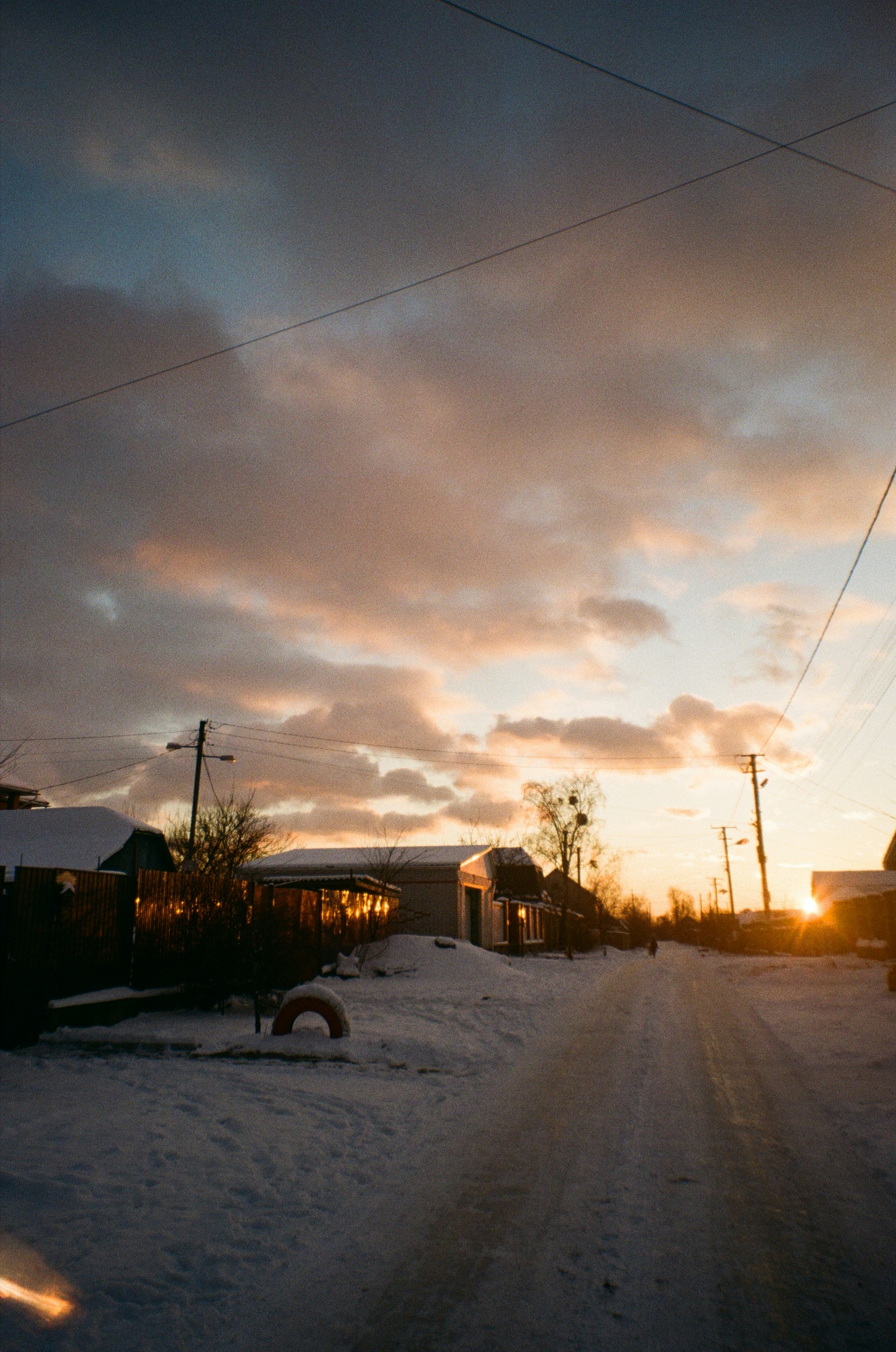 the sun is setting on a snowy street