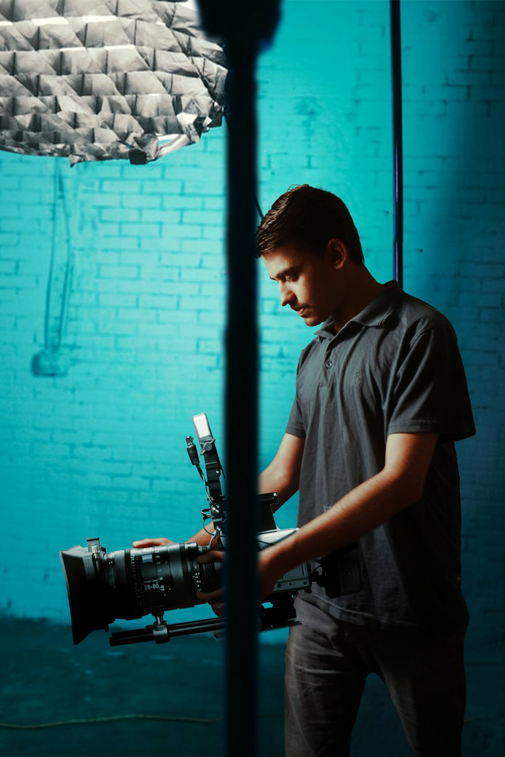 a man holding a camera in front of a blue brick wall