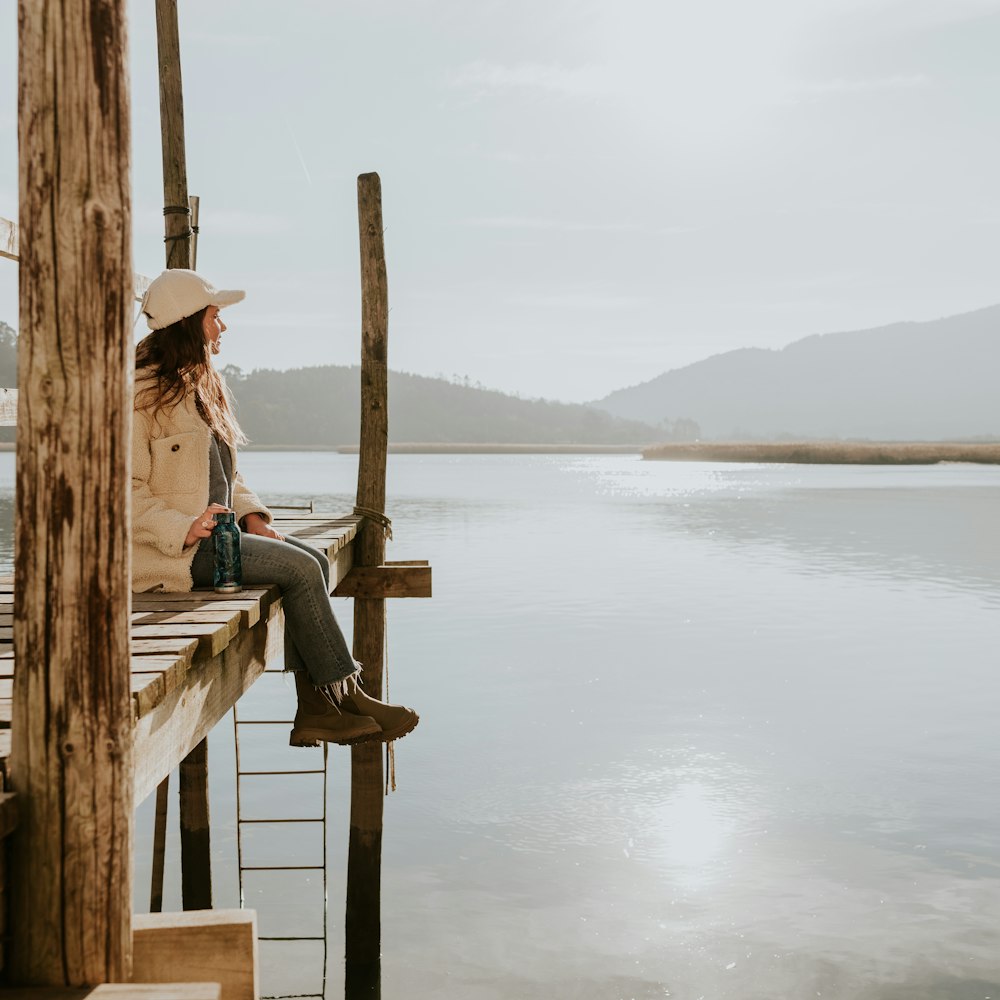 a woman sitting on a dock next to a body of water