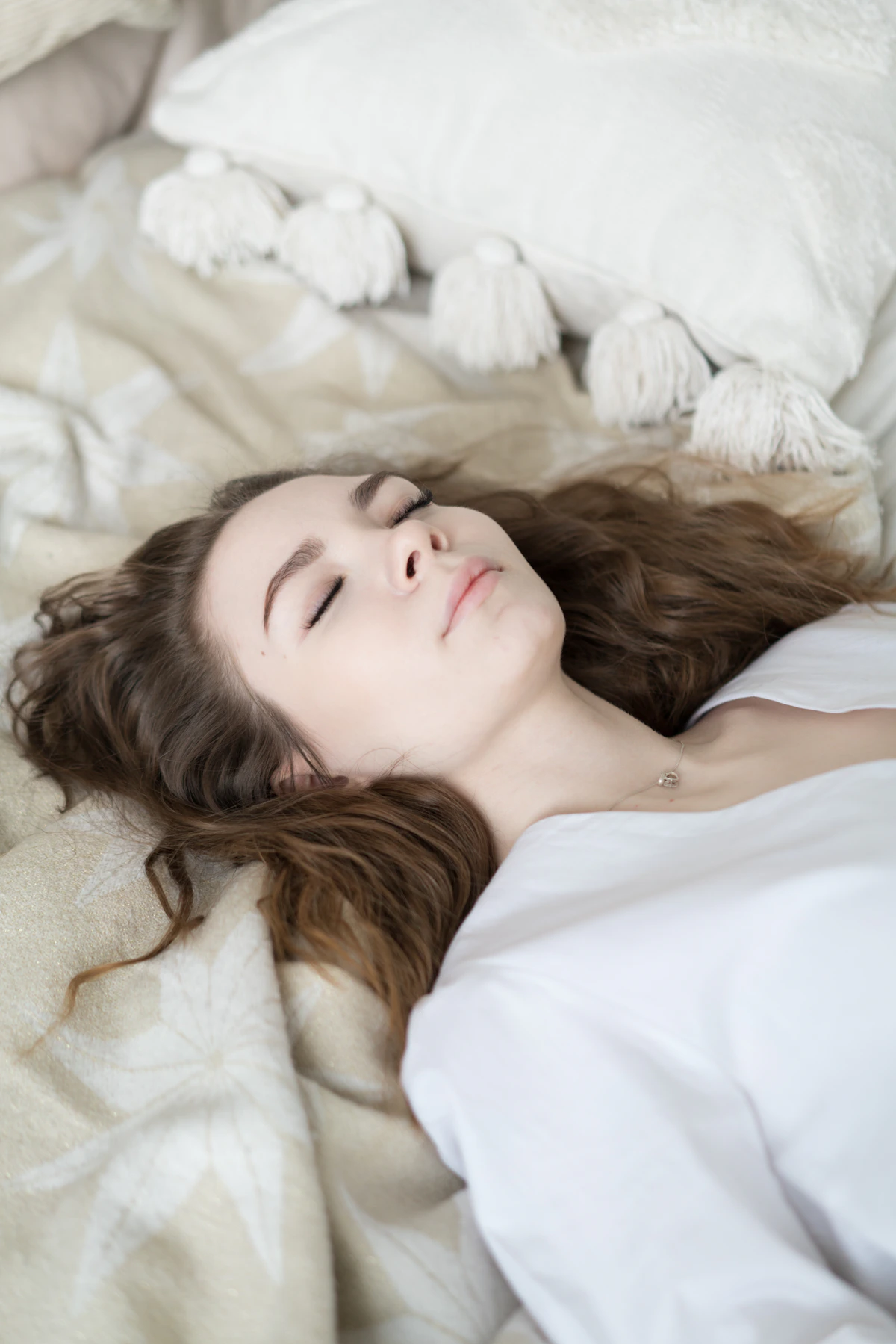 Vrouw rust met gesloten ogen onder zacht beddengoed, diepe drukstimulatie voor ontspanning en slaap