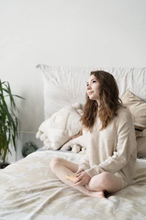 a woman sitting on top of a bed next to a plant