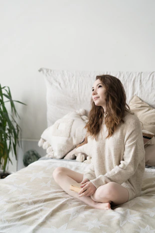 a woman sitting on top of a bed next to a plant