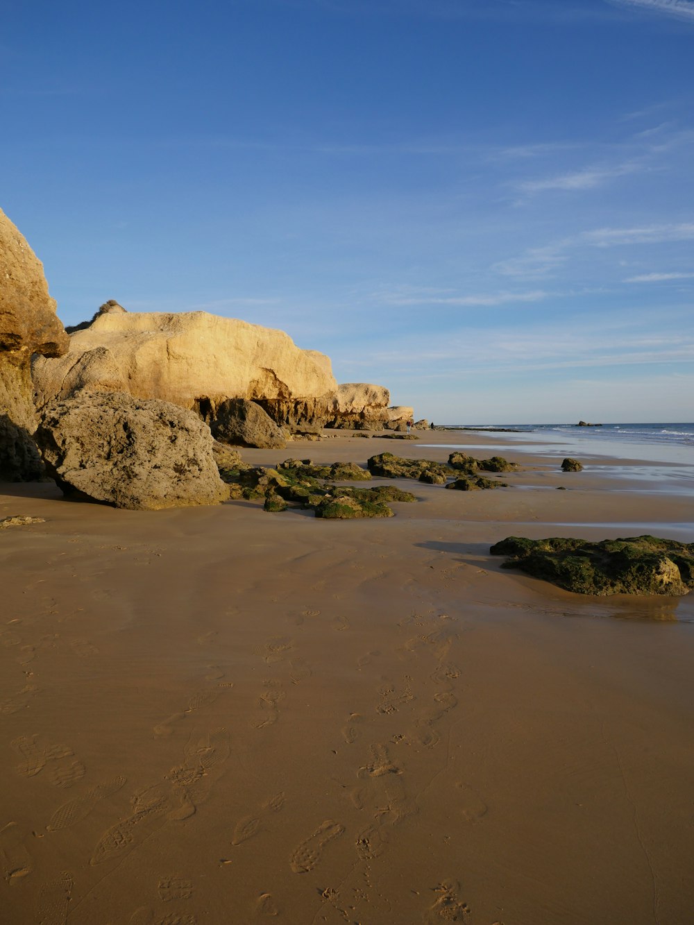 a sandy beach with rocks and water on a sunny day