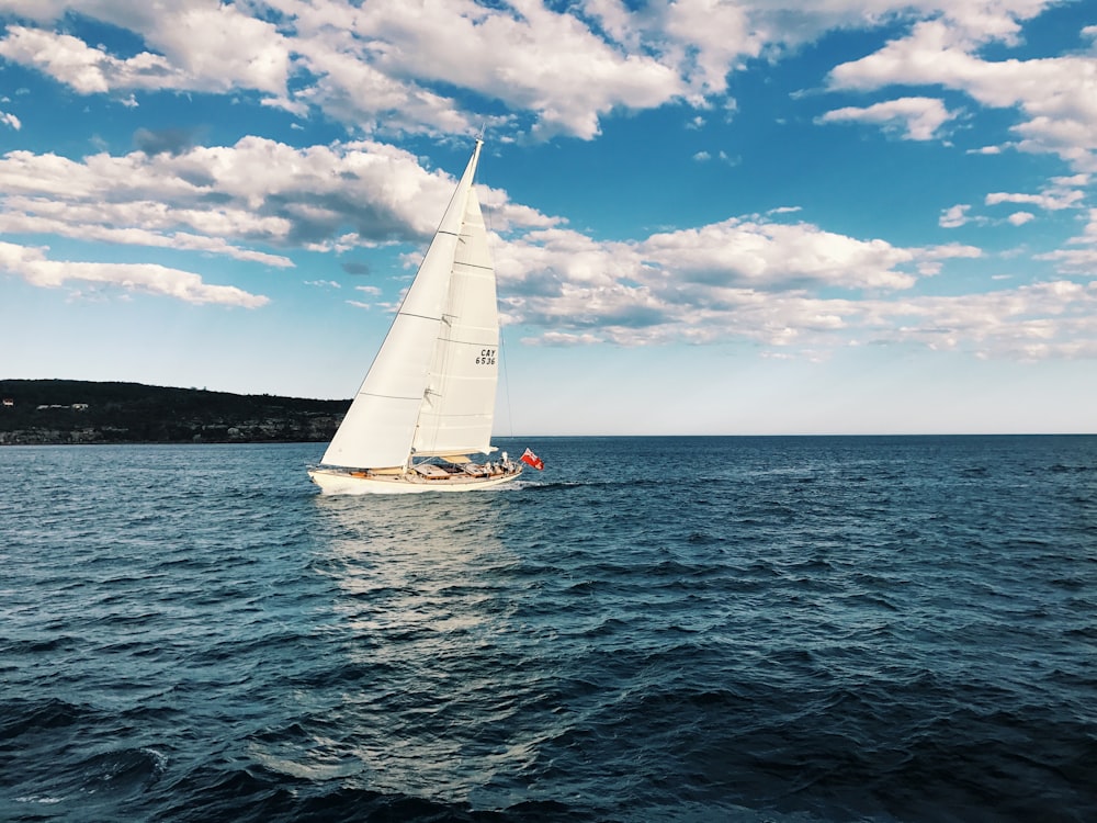 a sailboat sailing on the ocean under a cloudy blue sky