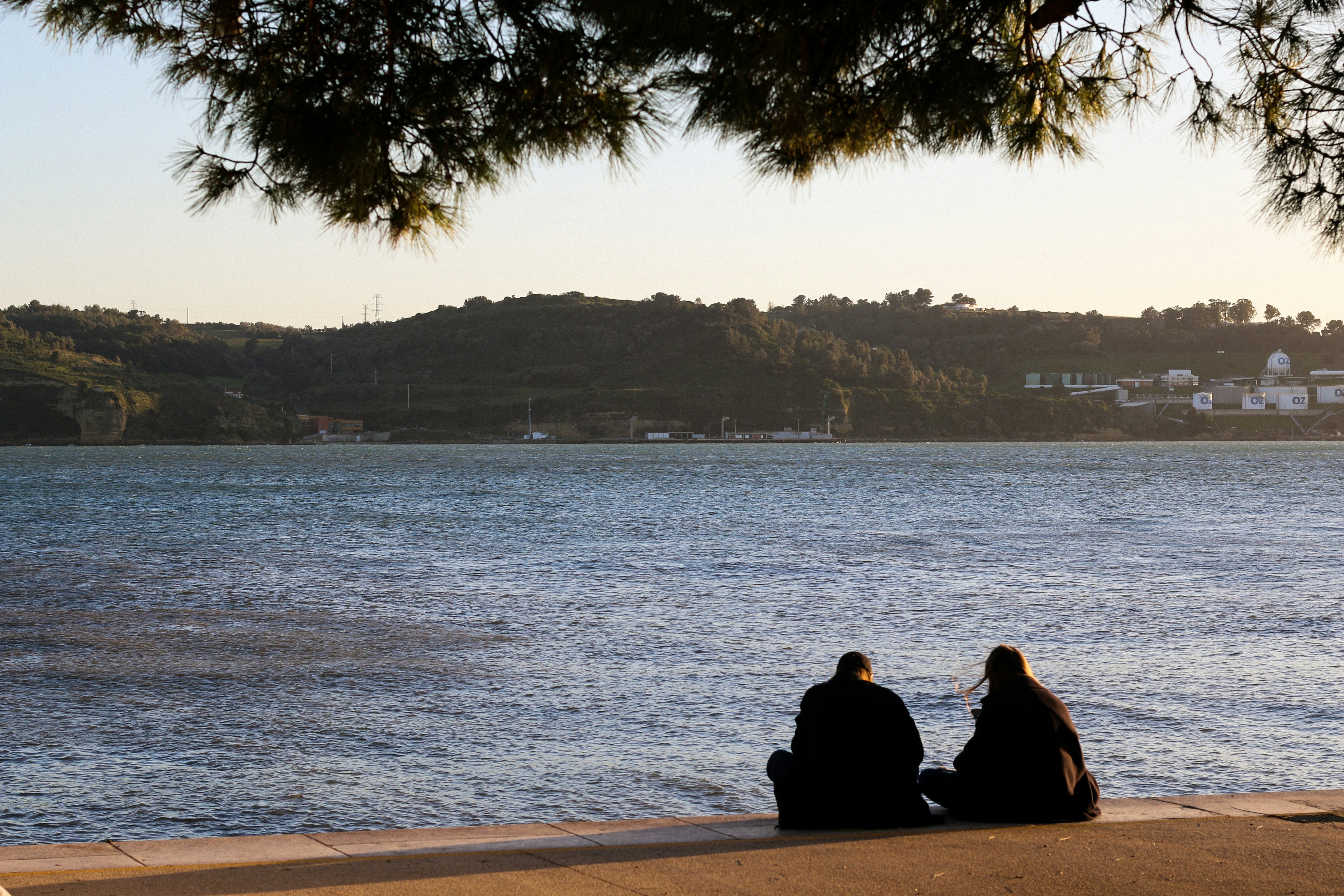 two people sitting on the edge of a body of water