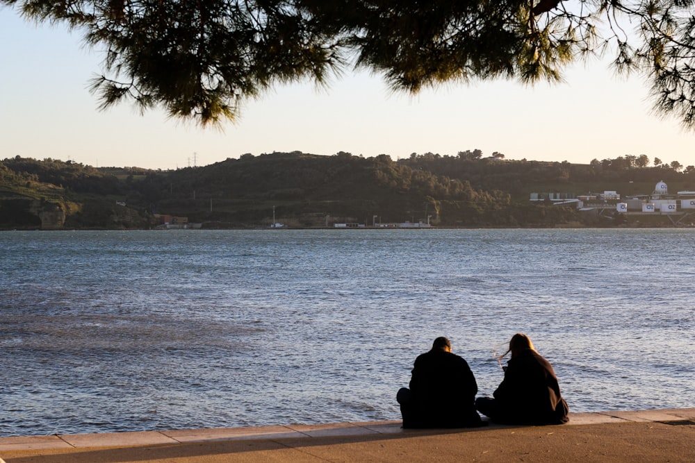 two people sitting on the edge of a body of water