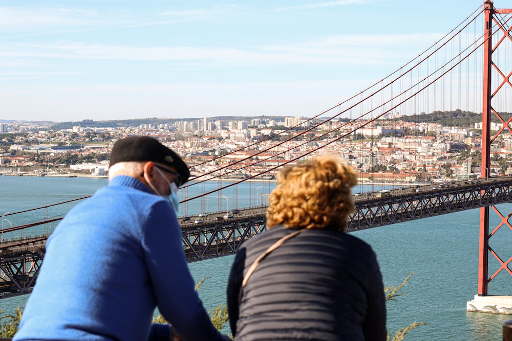 a man and a woman sitting on a bench looking at a bridge