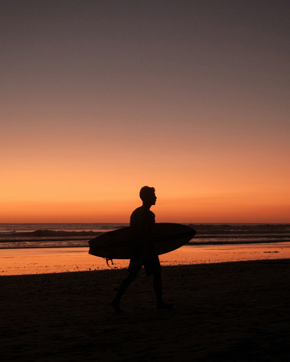 a man walking on a beach holding a surfboard