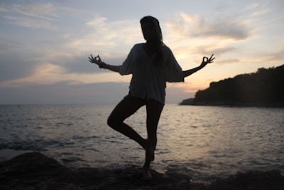 Rounded card with a light aqua background showing a tranquil yoga pose by the ocean at sunrise.
