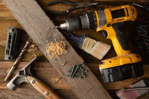 Power drill and hand tools laid on a wooden board