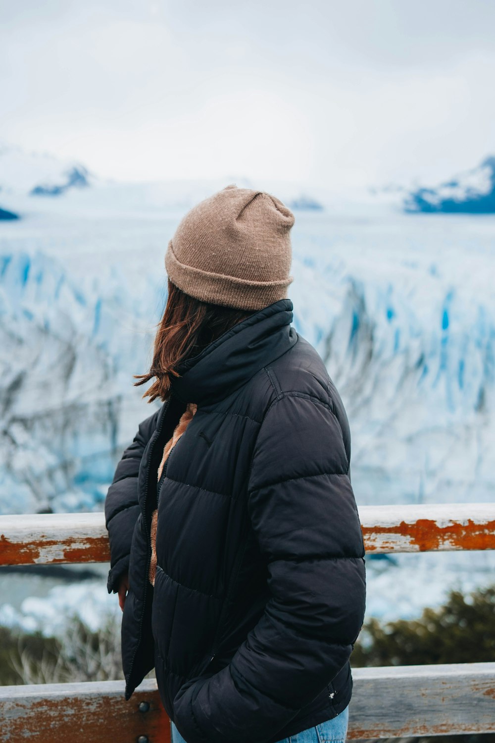 a woman standing on a railing looking at a glacier