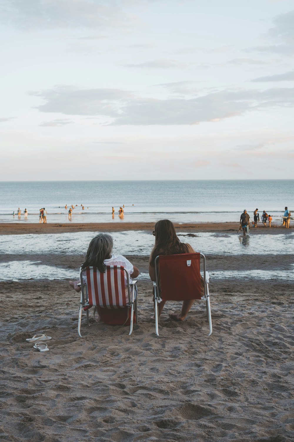 two people sitting in lawn chairs on a beach