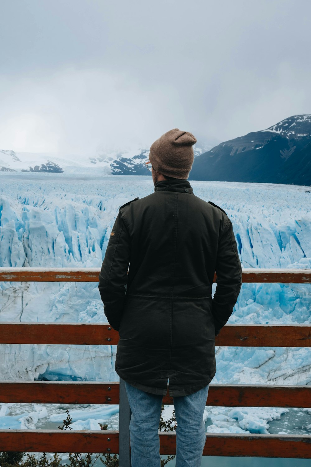a man standing on a bridge looking at a glacier