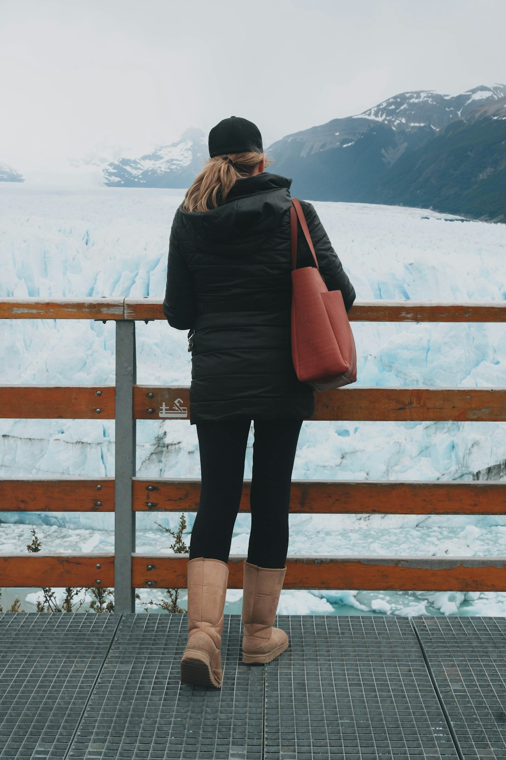 a woman standing on a bridge looking at a glacier
