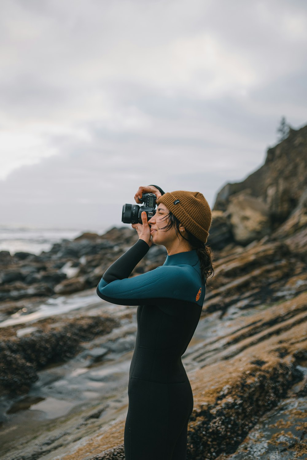 a woman standing on a rocky beach taking a picture