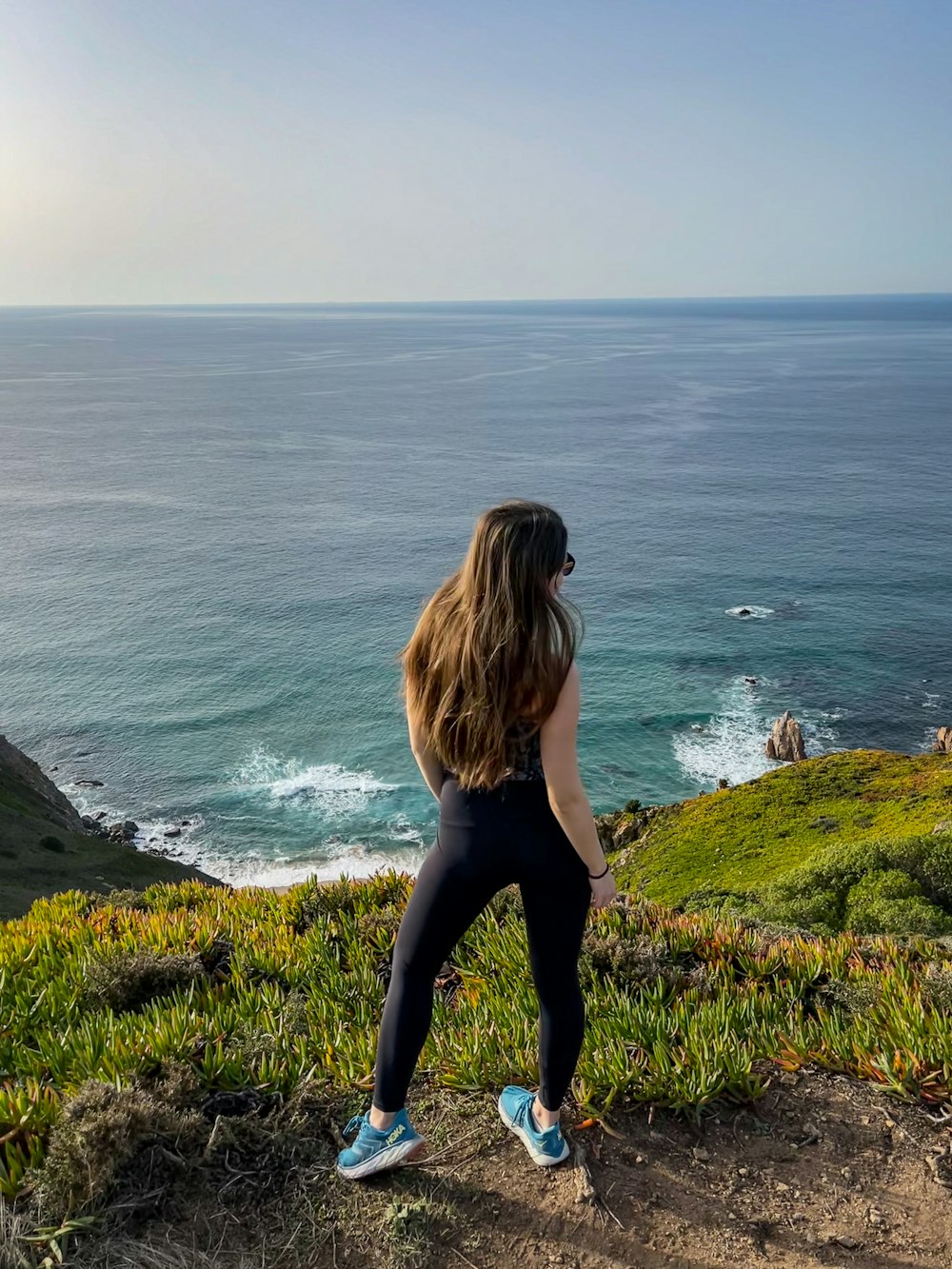 uma mulher de pé no topo de uma colina ao lado do oceano