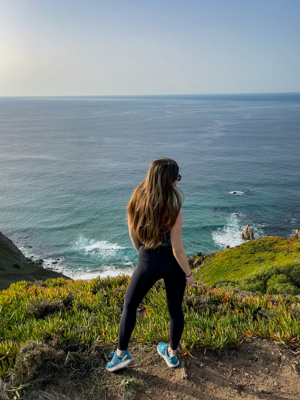 a woman standing on top of a hill next to the ocean