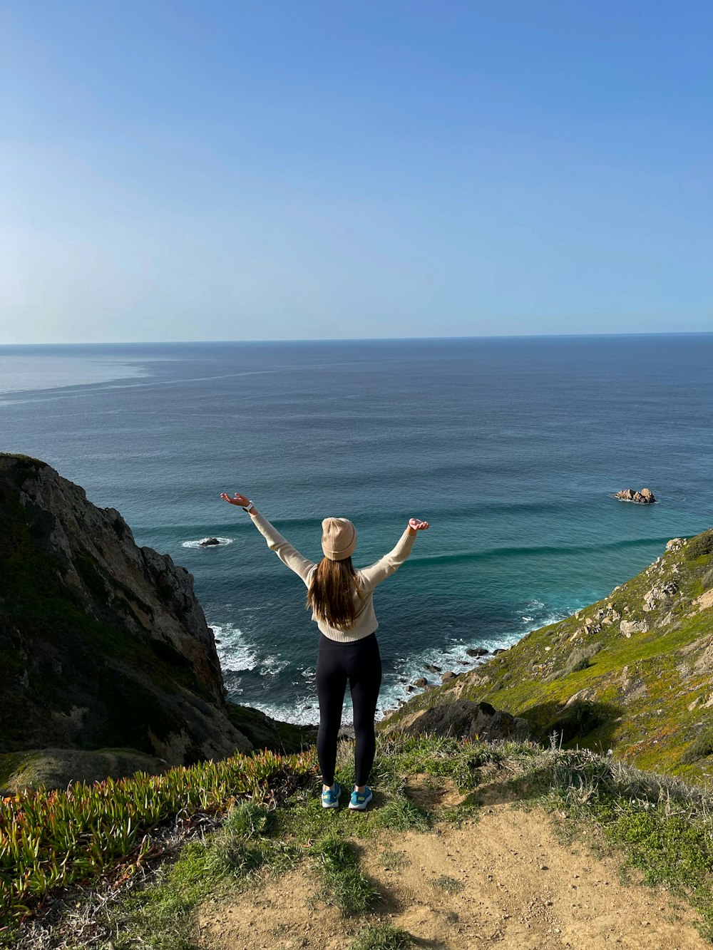 a woman standing on top of a hill next to the ocean