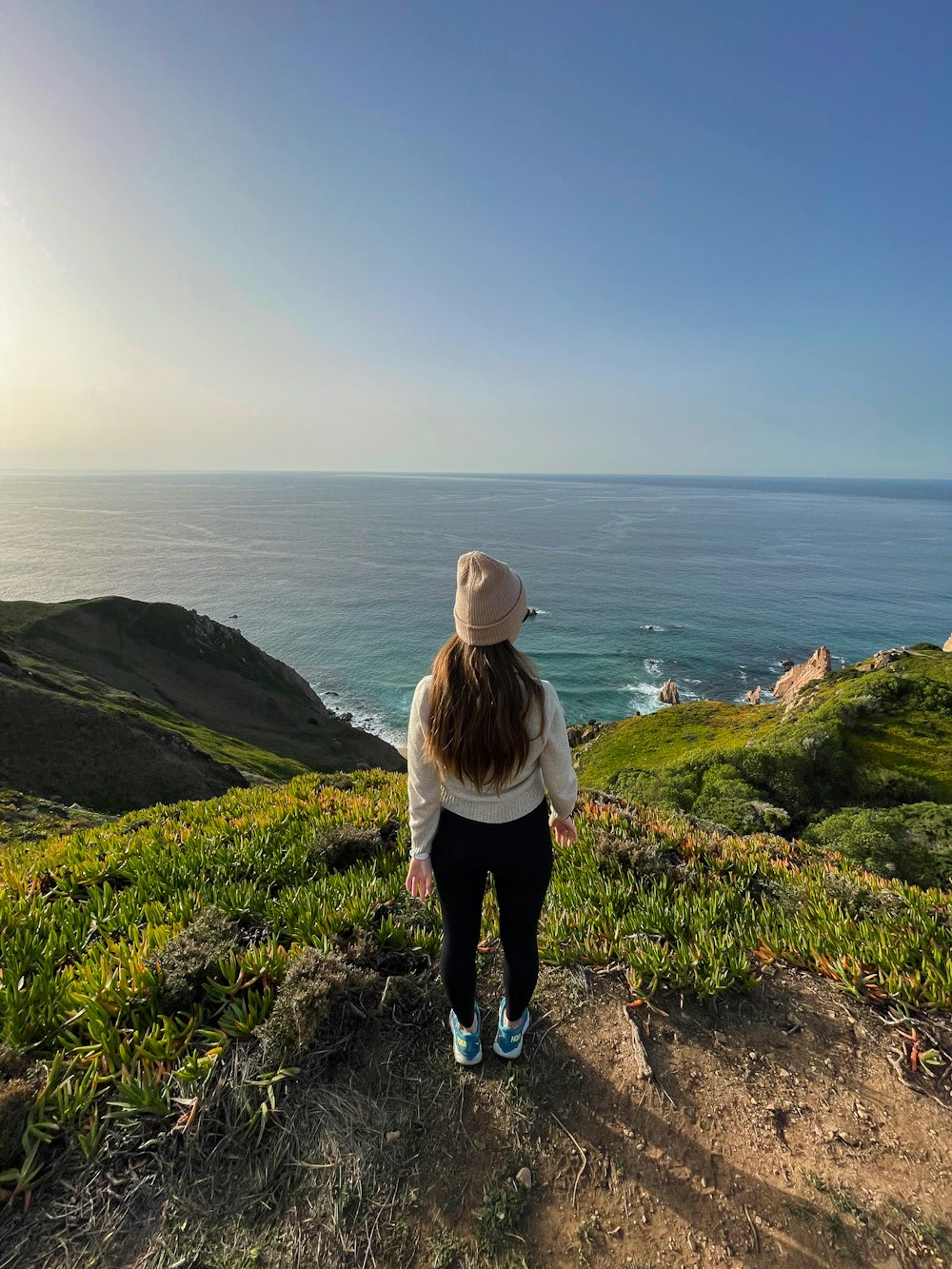 a woman standing on top of a lush green hillside