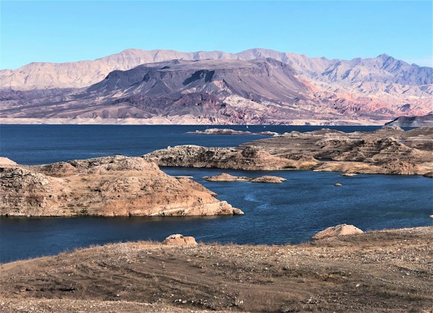 Rocky shoreline and coves of Lake Mead with desert mountains in the background on a clear day