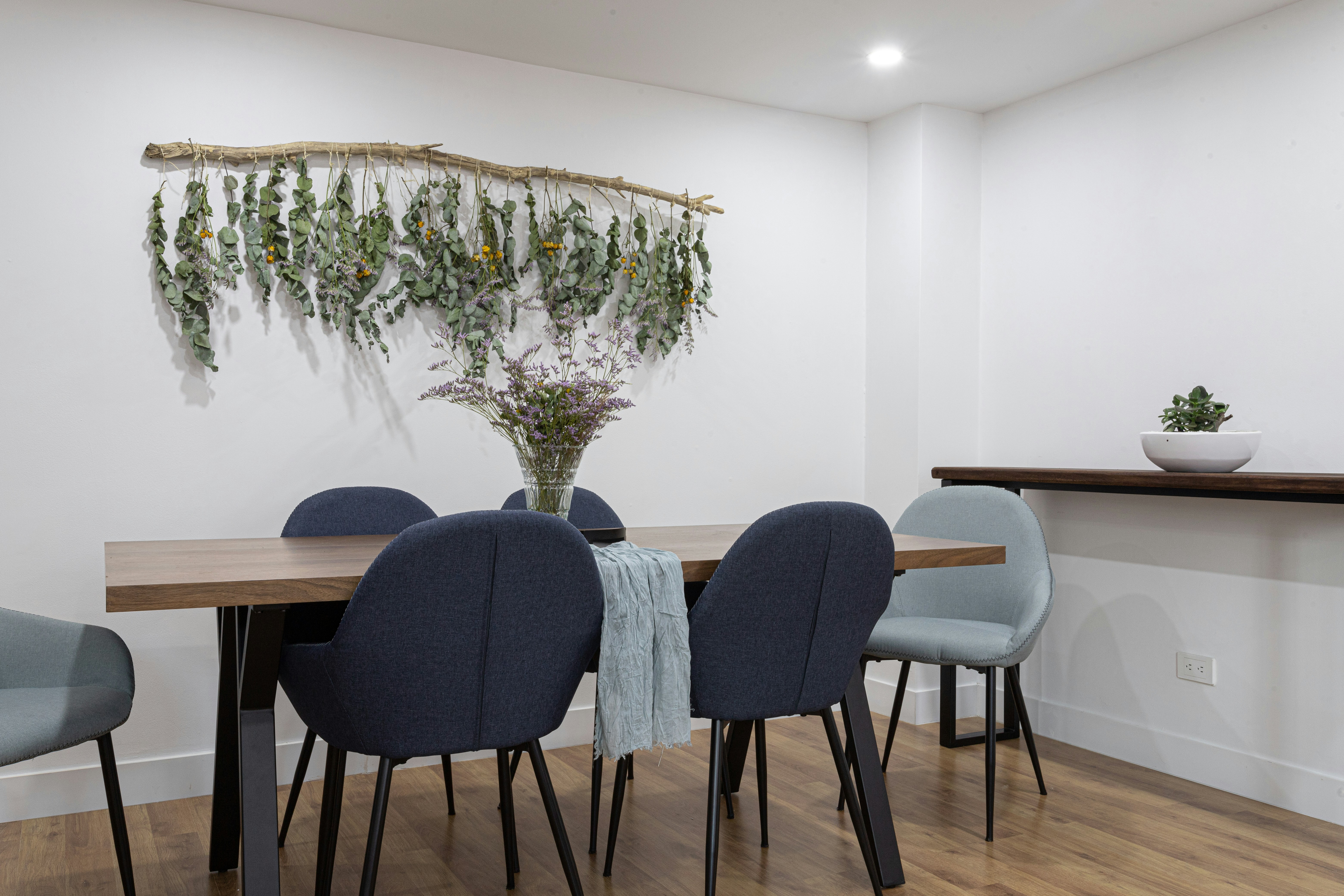 uma mesa de jantar com cadeiras azuis e uma planta pendurada na parede