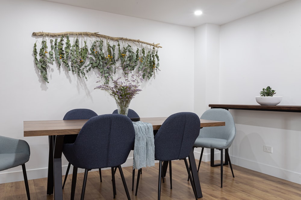 a dining room table with blue chairs and a plant hanging on the wall