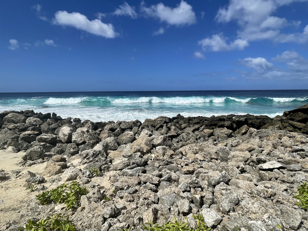 a rocky beach next to the ocean under a blue sky