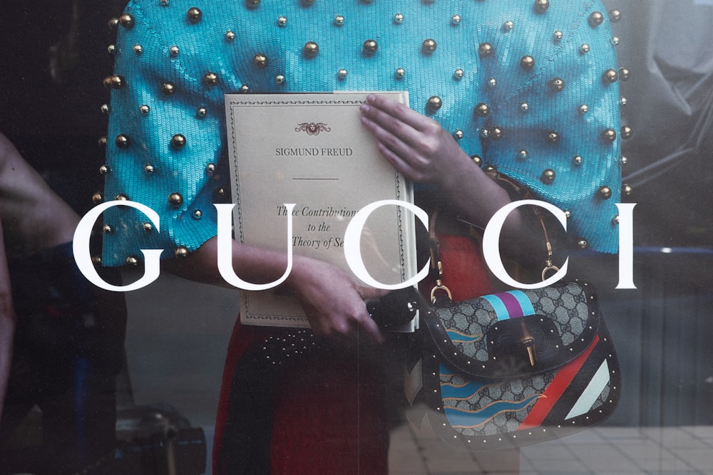 a woman holding a gucci bag in front of a window