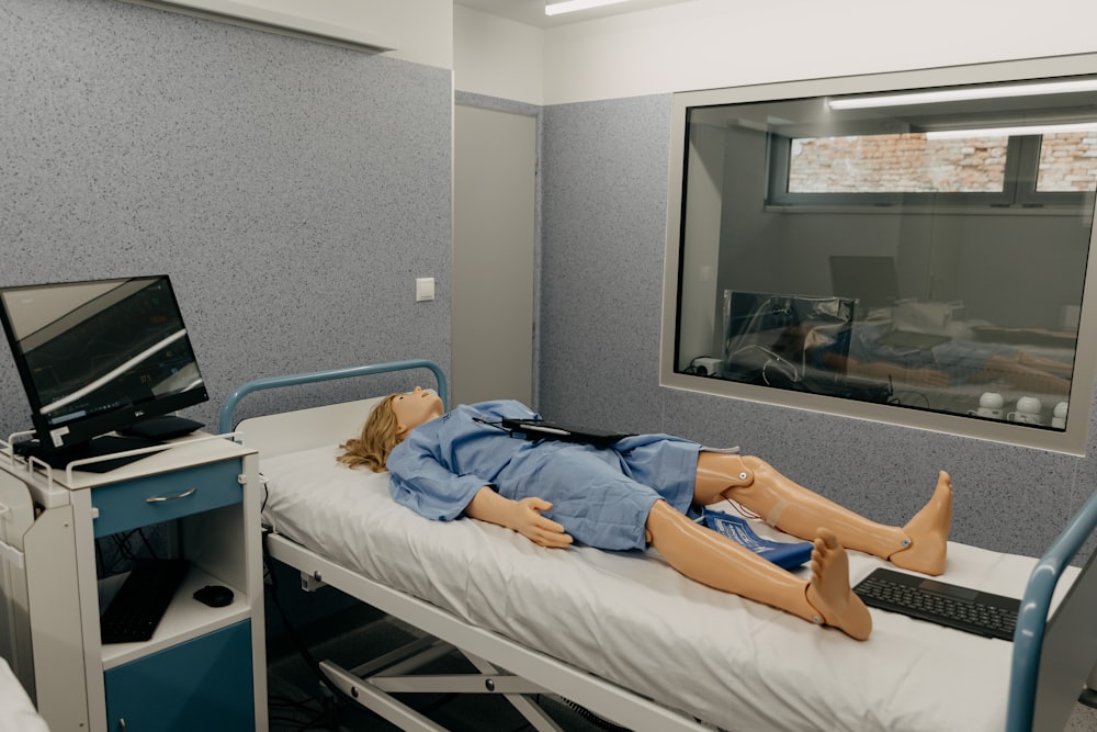 un maniquí acostado en una cama de hospital junto a un monitor
