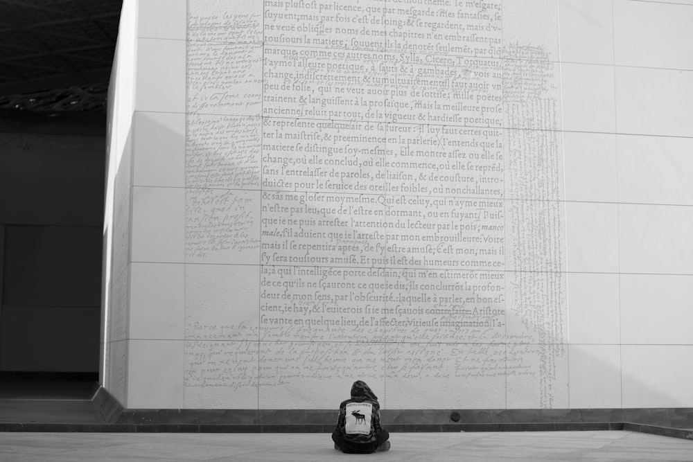 a black and white photo of a person sitting in front of a wall