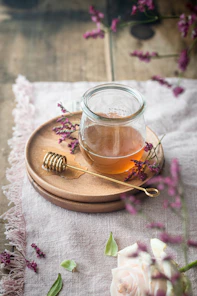 A close-up of a honey jar with a wooden dipper surrounded by fresh wildflowers on a rustic wooden table.