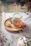 Close-up of a jar of golden honey with a wooden dipper resting on a rustic wooden table surrounded by fresh wildflowers.