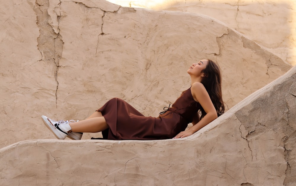 a woman in a brown dress sitting on a rock