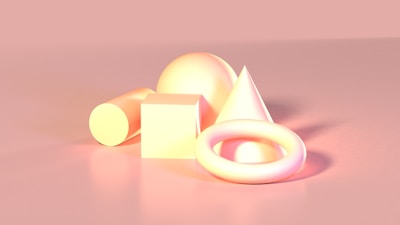 Several geometric shapes including a cylinder, cube, sphere, cone, and torus are arranged together on a smooth surface. The shapes are illuminated by a soft light, giving them a glowing appearance. The overall color scheme is a warm gradient, primarily consisting of pastel pinks and yellows.