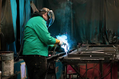 a man in a green jacket welding a piece of metal
