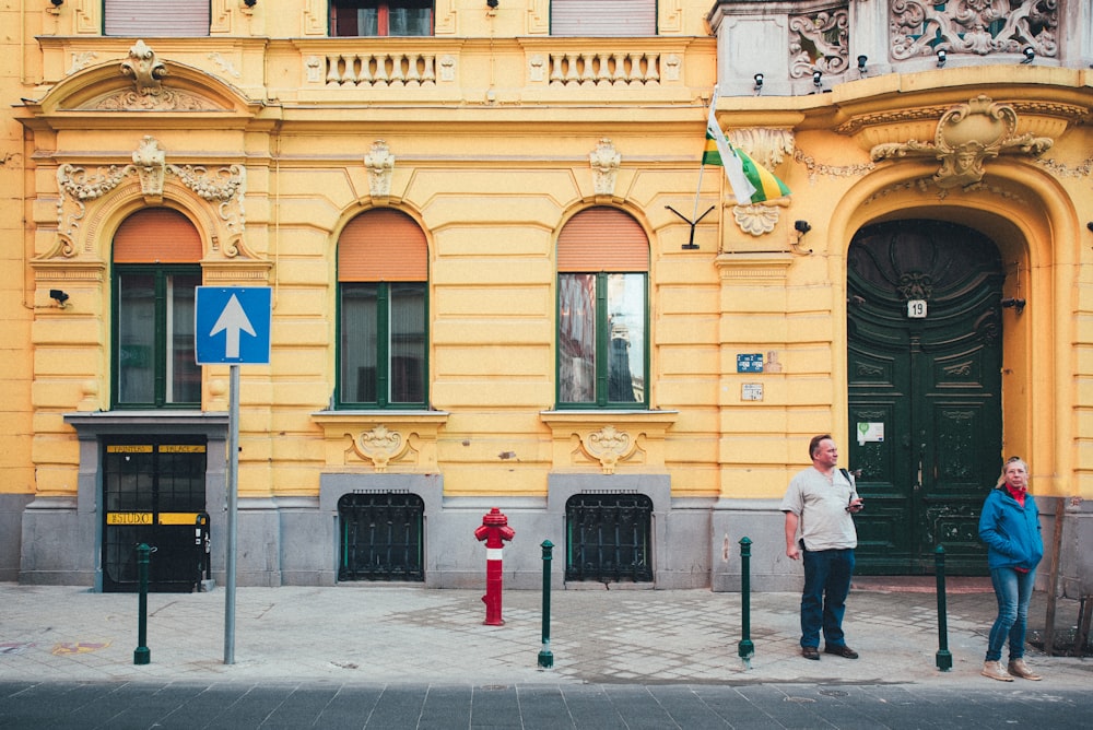 two people standing in front of a yellow building