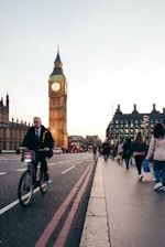 a man riding a bike down a street next to a tall clock tower