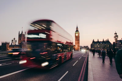 a red double decker bus driving down a street Britain