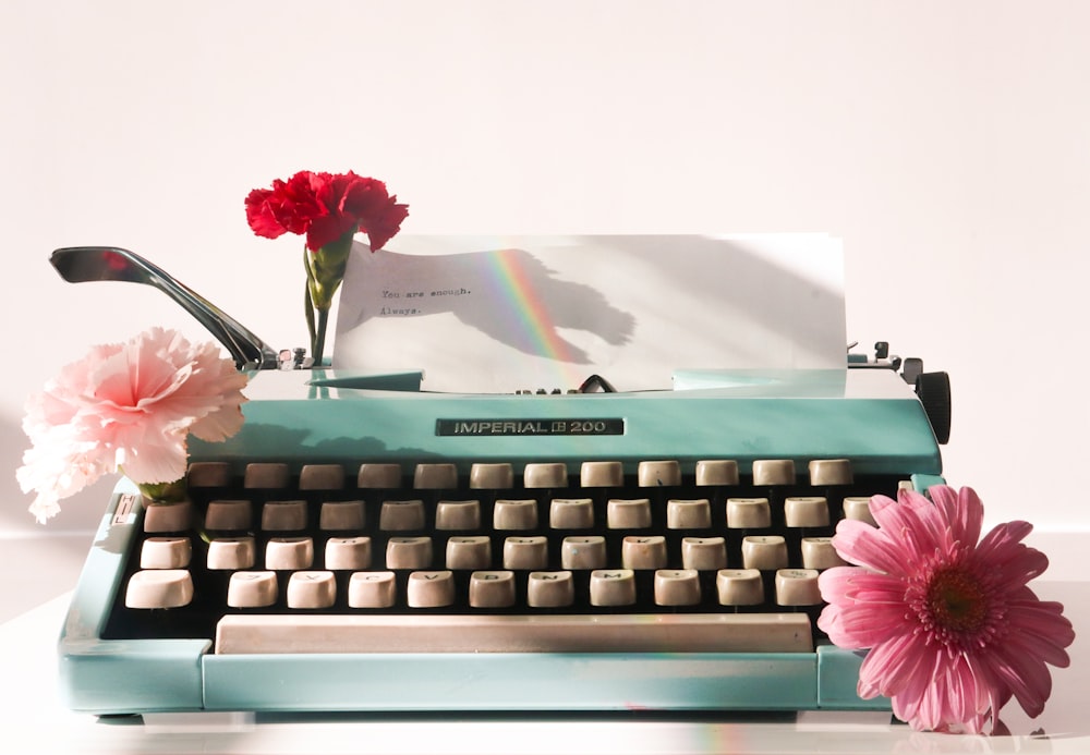 a pink flower sitting on top of a blue typewriter