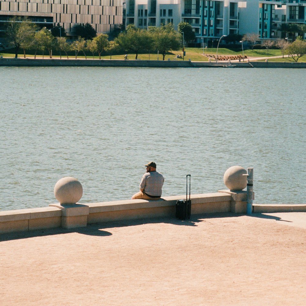 a man sitting on a wall next to a body of water