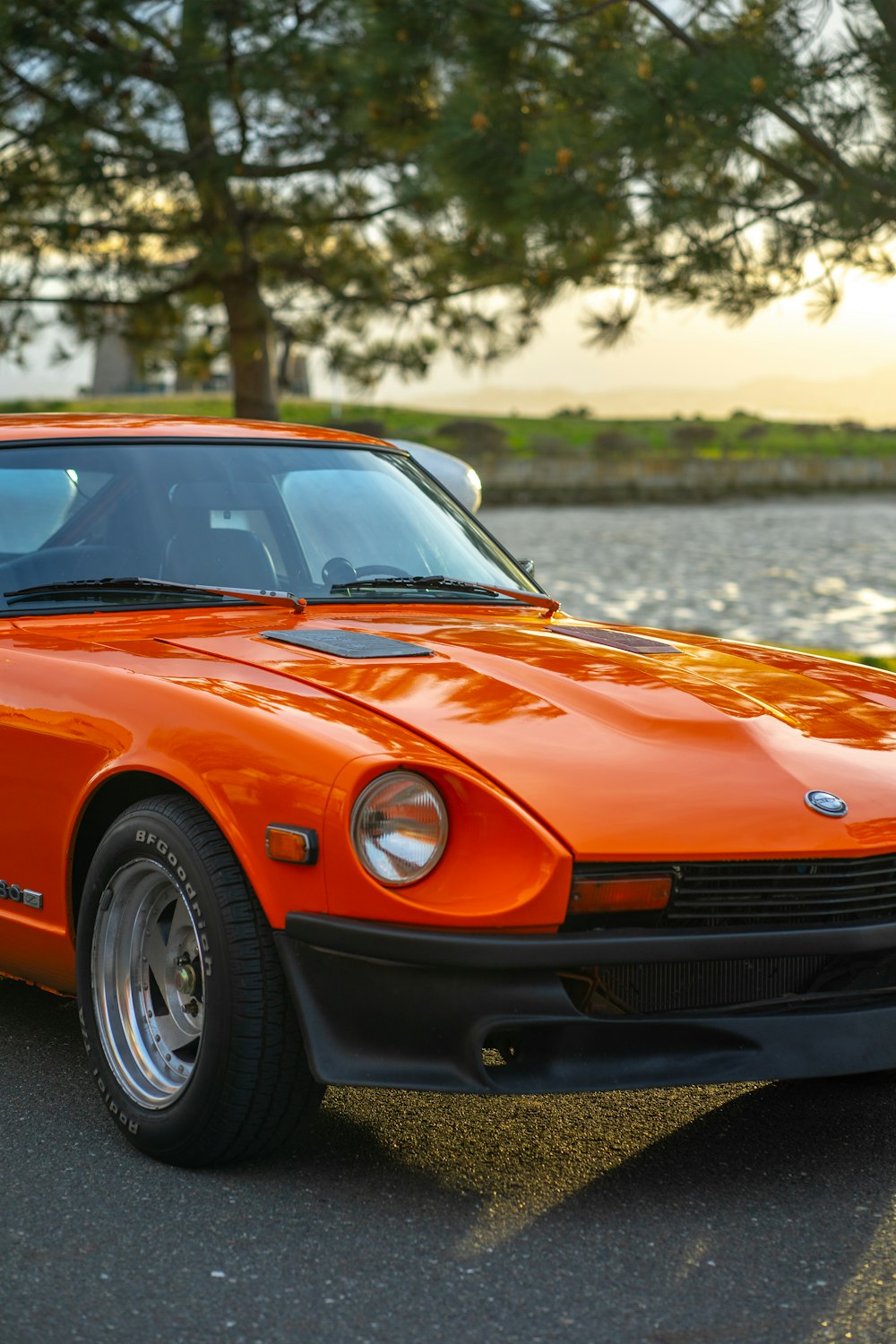 an orange sports car parked in front of a body of water