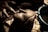 A hand is carefully sculpting a clay face, capturing fine details and expressions. The setting appears dimly lit, with shadows enhancing the intricate textures of the clay.