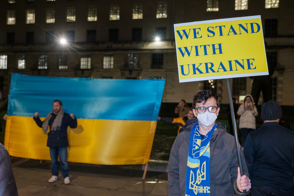 a man holding a sign that says we stand with ukraine