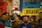 A group of people holding signs and banners in support of Ukraine. The central sign has bold letters saying 'Stand with Ukraine.' There are various other signs and flags visible, with people of diverse backgrounds participating in the gathering.