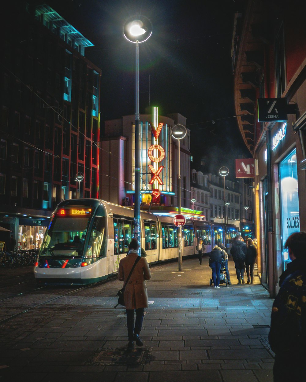 a city street at night with people walking on the sidewalk