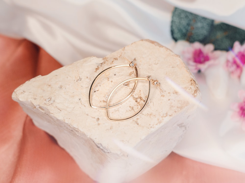 a pair of gold hoop earrings sitting on top of a rock