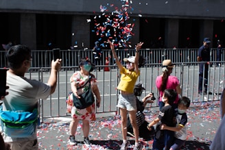 Colorful children and parents joyfully throwing confetti at a school event outdoors.