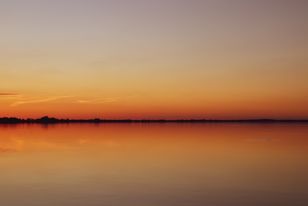 the sun is setting over a calm lake