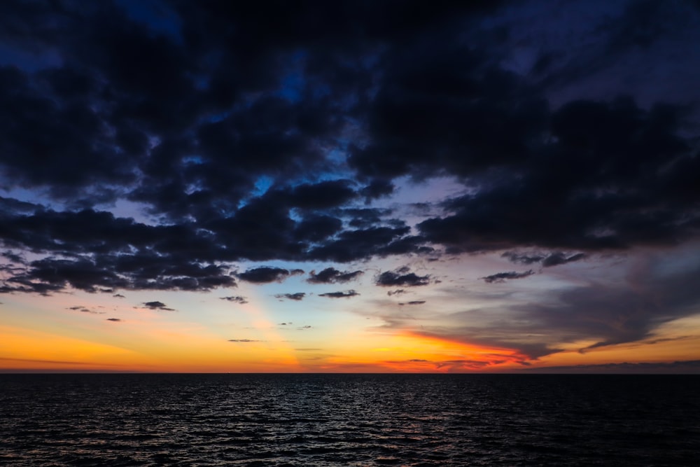 the sun is setting over the ocean on a cloudy day